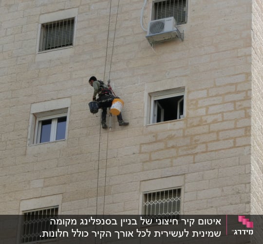 אדם תלוי על חבלים עם דליים על קיר בניין